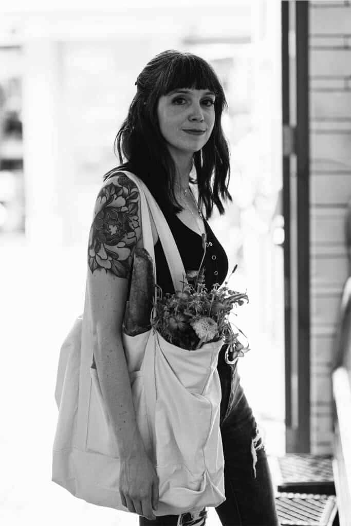 A woman holding a bag of food and flowers.