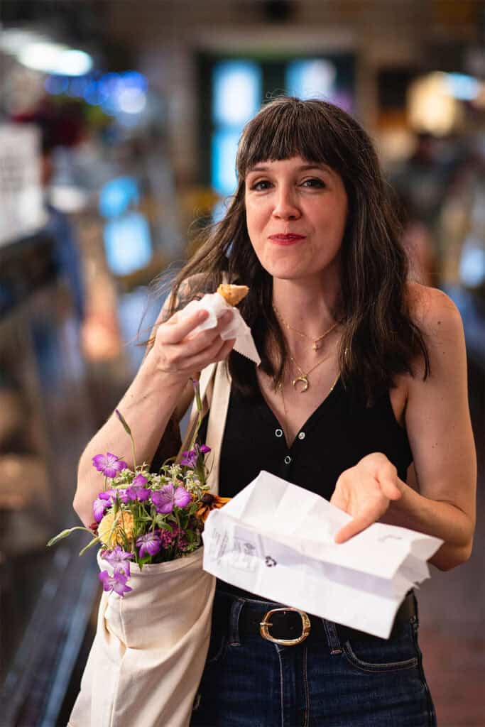 A woman holding a bag of food and flowers.