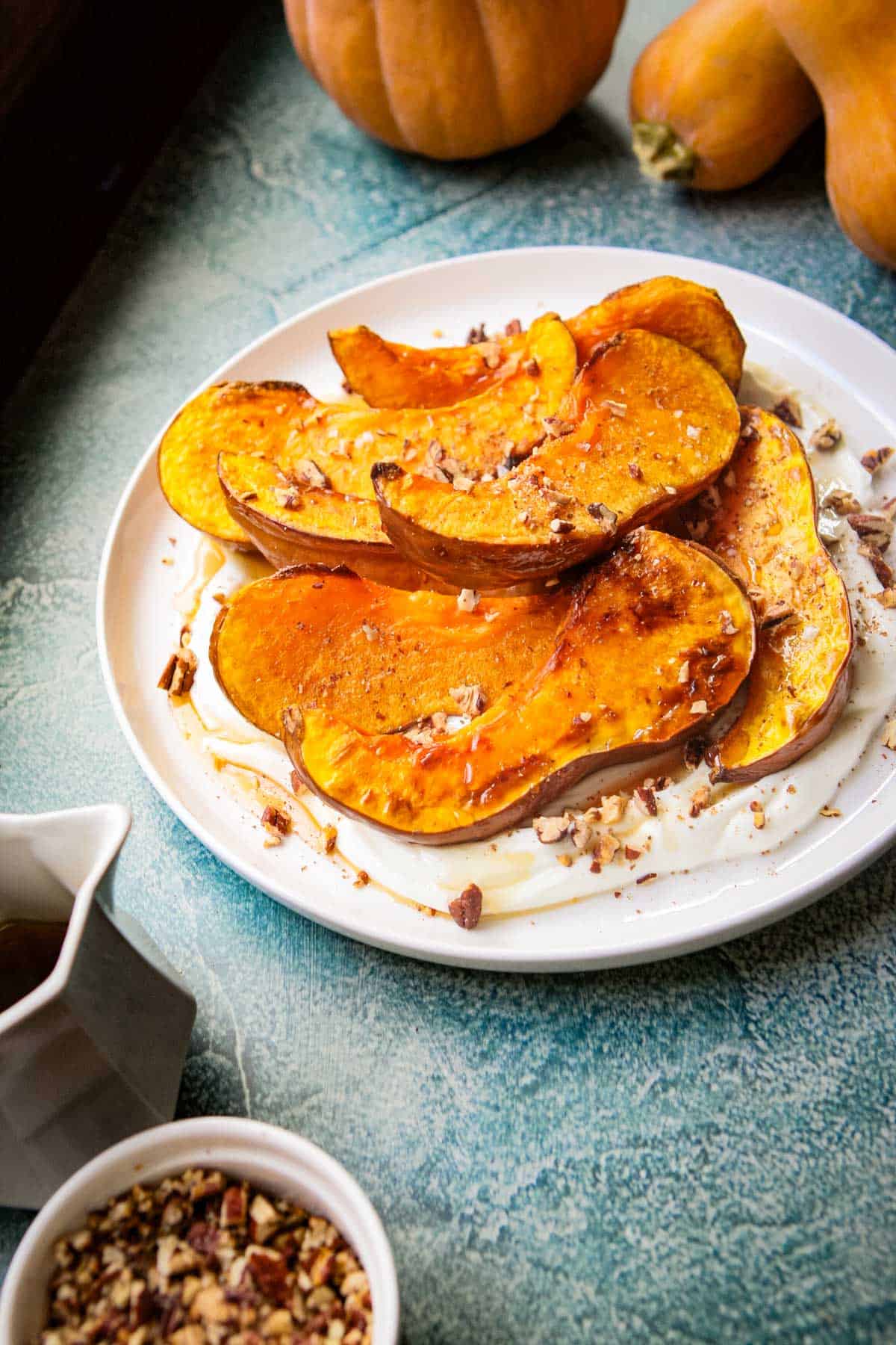 a plate of squash with a cup of maple and bowl of nuts
