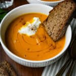 a bowl of carrot soup with bread