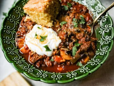 a bowl of chili with cornbread nearby